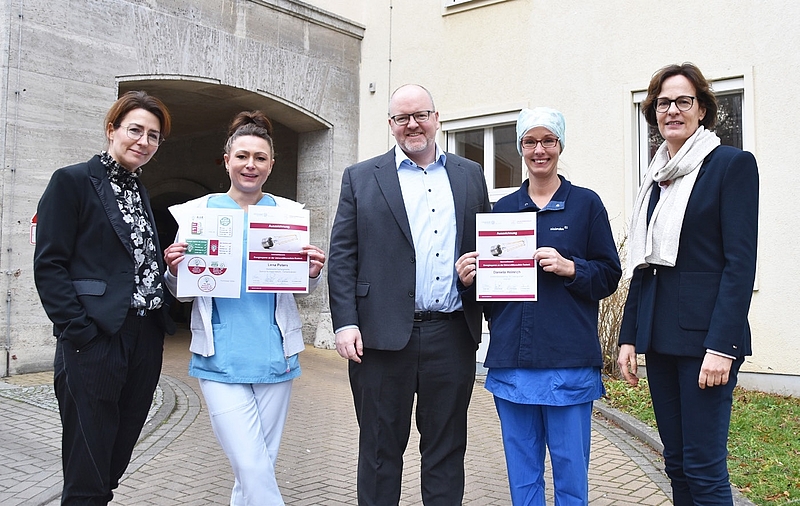 Fünf Menschen stehen vor dem Eingang der Kinderklinik der Unimedizin Rostock. Zwei Krankenschwestern in Berufskleidung halten Urkunden in den Händen. Der Energiesparwettbewerb dient der Nachhaltigkeit.