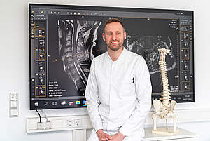 Porträt von Dr. Florian Geßler neben einem Wirbelsäulenmodell 