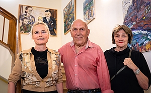 Zwei Frauen und ein Mann stehen auf einer Treppe, im Hintergrund hängen Ölgemälde