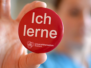 Mitarbeiterin hält Button mit der Aufschrift "Ich lerne" in die Kamera