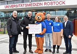 Teddy-Docs und Spender stehen mit einem Spendenscheck vor dem Haupteingang