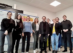 Gruppe von acht Personen steht vor zwei mit bunten Zetteln beklebten Whiteboards in einem Büro