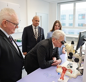 Joachim Gauck schaut in ein Mikroskop, weitere Teilnehmer stehen um ihn herum