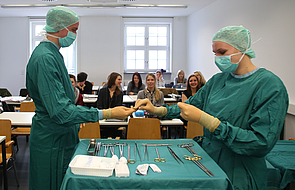 Zwei Operationsassistenten in grüner OP-Bekleidung üben in einem Seminarraum mit OP-Instrumenten
