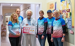 Fünf Männer und Frauen in blau-roten Laufshirts mit Arzt und Spendenscheck
