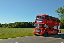 Ein roter Doppeldeckerbus fährt auf einer Landstraße.