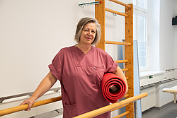 Physiotherapieleiterin Imke Albrecht hält eine zusammengerollte Matte unter dem Arm und lehnt an einem Geländer