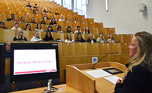 Neue Pflegeazubis sitzen im Hörsaal, Caren Erdmann vorne im Podium