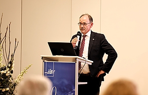 Ein Mann steht hinter einem Rednerpult und hält ein Mikrofon in der Hand.