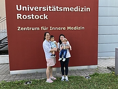 Zwei junge Frau halten jeweils ein Baby auf dem Arm und stehen vor einem Klinikgebäude
