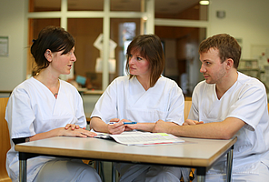 Drei Pflegekräfte in weißen Kasacks sitzen zur Beratung an einem Tisch