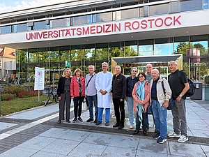 Gruppe von neun Personen steht vor dem Gebäude der Universitätsmedizin Rostock, eine Person trägt einen weißen Arztkittel