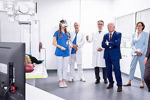 Eine Person trägt eine VR-Brille, 4 andere Personen schauen ihr zu.