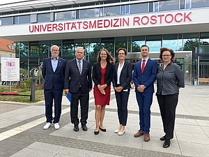 Sechs Menschen in Bussinesskleidung stehen vor einem Klinikgebäude