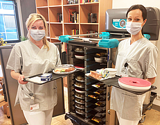 Assistentin Adina Lenz (l.) und Christin Staniewska stehen mit Tabletts in der Hand vor einem Speisewagen