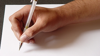 Hand hält Stift über weißem Blatt Papier