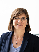 Frau mit dunklen, schulterlangen Haaren und Brille vor hellem Hintergrund