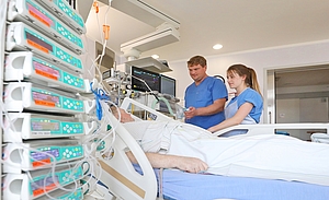 Bett mit Intensivpatient und zwei Personen in blauem Kasack