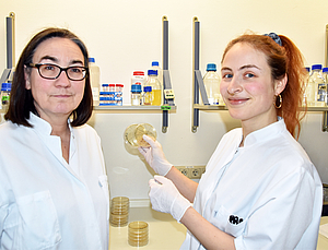 Zwei Frauen stehen im Labor. Die rechte Person hält eine Petrischale in die Luft