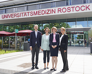 Vier Personen im Businesslook stehen vor dem Haupteingang der Universitätsmedizin Rostock