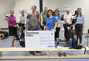 9 Personen befinden sich in einem Sportraum und halten einen Spendenscheck in der Hand.