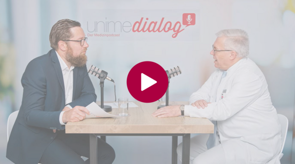 Zwei Personen sitzen an einem Tisch mit Mikrofonen und führen ein Gespräch, in der Mitte ein rotes Wiedergabesymbol
