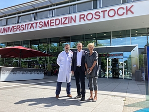 Zwei Männer und eine Frau stehen vor einem Gebäudeeingang