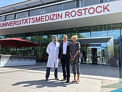 Zwei Männer und eine Frau stehen vor einem Gebäudeeingang