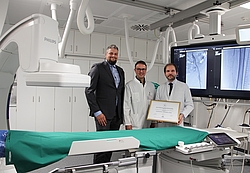 Drei Männer in einem Untersuchungsraum mit einem CT-Gerät