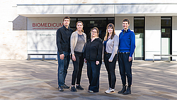 Eine Gruppe aus fünf Personen steht vor einem Gebäudeeingang