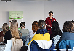 Prof. Dorothea Tegethoff steht vor einem Publikum und hält eine Rede vor sitzenden Studenten