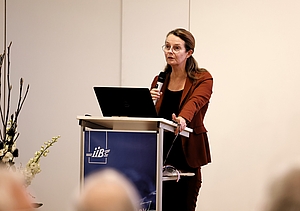 Eine Frau steht hinter einem Rednerpult und hält ein Mikrofon in der Hand.