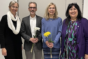 Vier Personen nebeneinander, zwei davon mit Blumen 