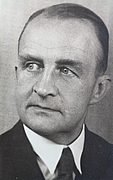 schwarz-weißes Porträtfoto eines Mannes im schwarzen Jacket mit weißem Hemd und dunkler Krawatte