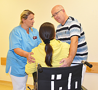 Pflegekraft und Mann helfen Frau mit Zopf aus Rollstuhl