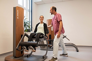 Patient übt unter Anleitung eines Physiotherapeuten eine Übung an einem Fitnessgerät aus.