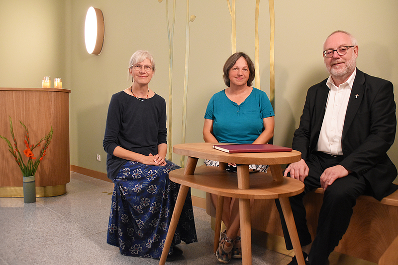 Zwei Pastorinnen und ein Pastor sitzen an einem Holztisch in einem hellgrünen Raum und einem Holzpult im Hintergrund. Die Krankenhausseelsorger ergänzen den Sozialdienst der Unimedizin Rostock.