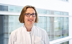 Frau mit kinnlagen Haaren und Brille vor hellem Hintergrund.