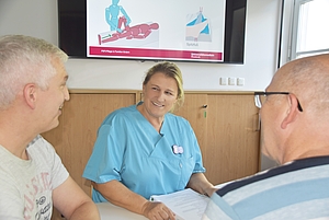 Eine lächelnde hellblau gekleidete Person erklärt 2 weiteren etwas.