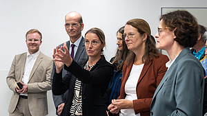 Viele Persone stehen nbeneinander und hören gespannt zu. Eine andere Person erklärt etwas.