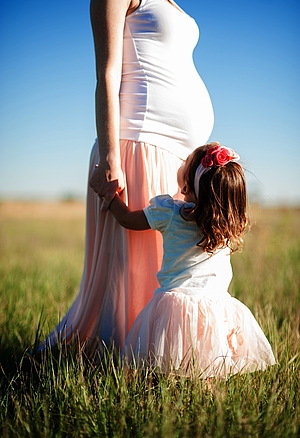 Schwangere Frau mit kleinem Mädchen auf einer Wiese
