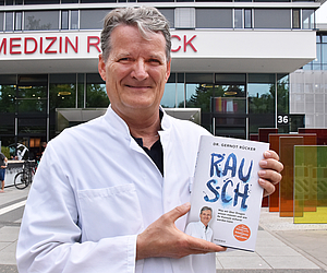 Dr. Gernot Rücker vor dem Haupteingang mit Buch in der linken Hand