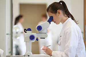 junge Frau in weißem Kittel an einem Mikroskop