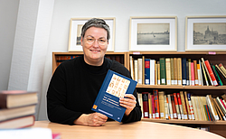 Frau mit kurzen Haaren sitzt am Tisch und hält Buch in der Hand