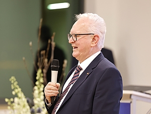 Ein Mann steht, hält eine Rede und spricht in ein Mikrofon