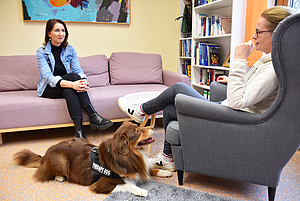 Zwei Frauen im Gespräch, ein Hund liegt auf dem Fußboden