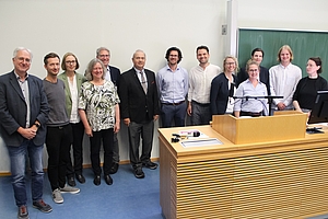 13 Personen stehen zusammen für ein Gruppenbild und schauen sehr freundlich.