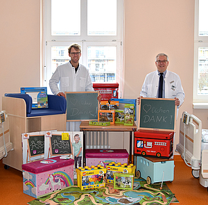 Dr. Thiem und Prof. Emmert stehen hinter einem Berg aus Spielzeug
