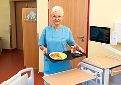 Schwester mit Tablett in der Hand vor einem Patientenbett