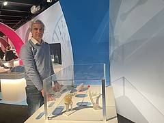 Mann in grauem Pullover und in Jeans an einer Glasvitrine, die Exponate enthält